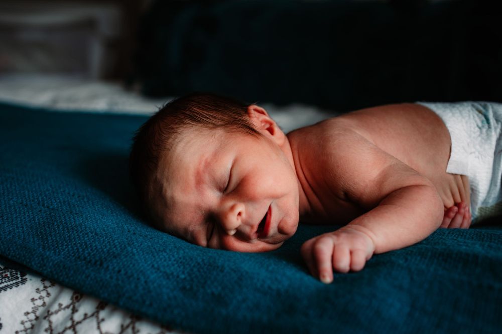 Peaceful newborn baby sleeping on blue blanket during professional photoshoot.