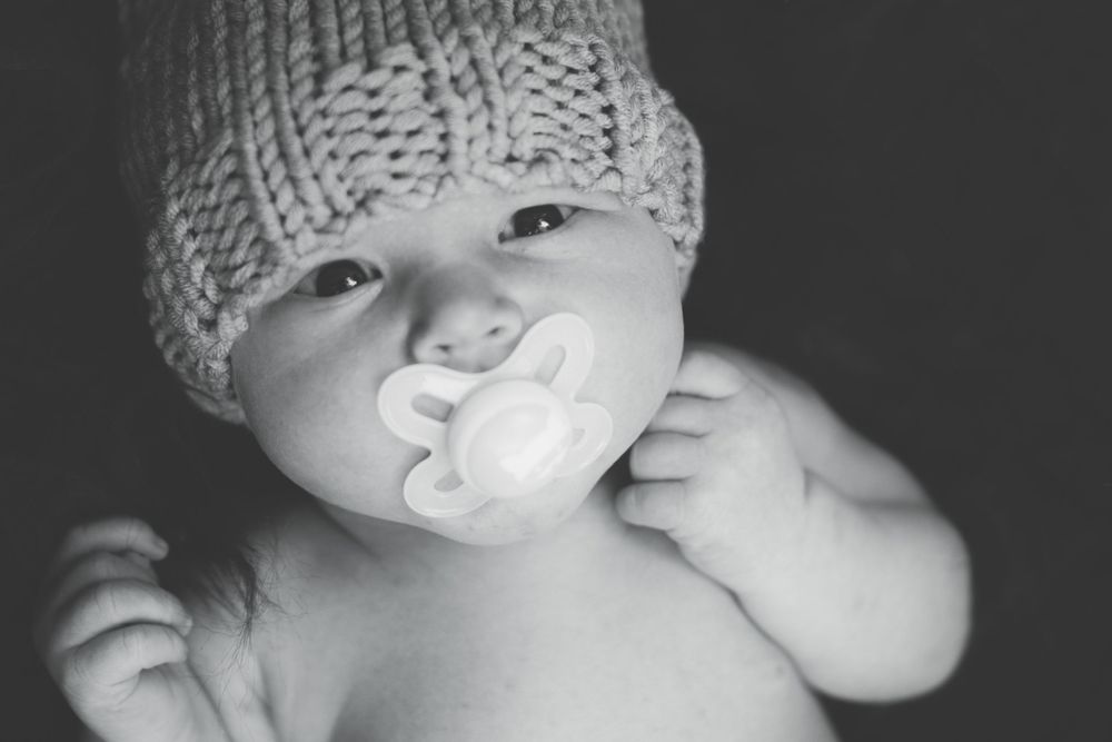 Close-up of baby wearing knit hat with pacifier in monochrome.