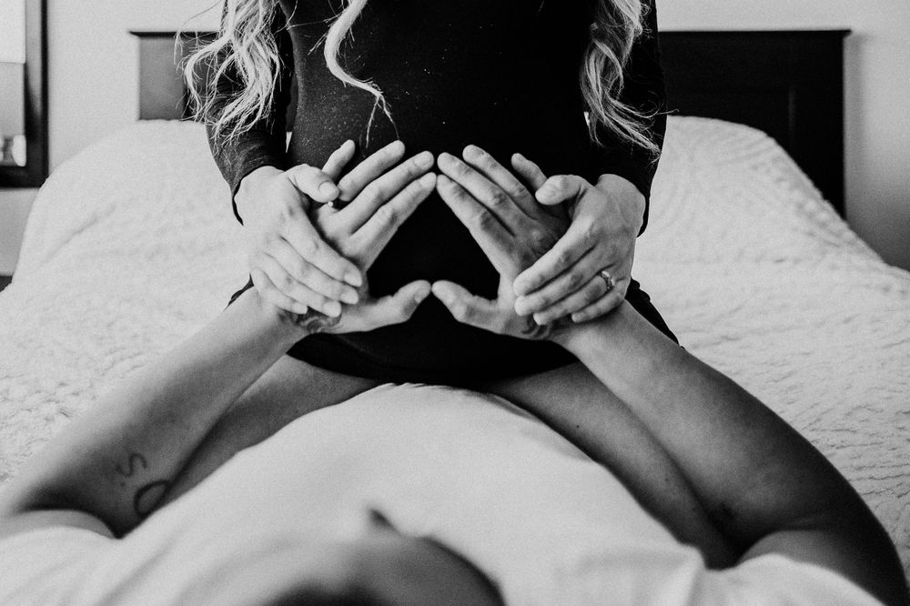 Black and white artistic maternity photo showing hands forming heart shape on belly.
