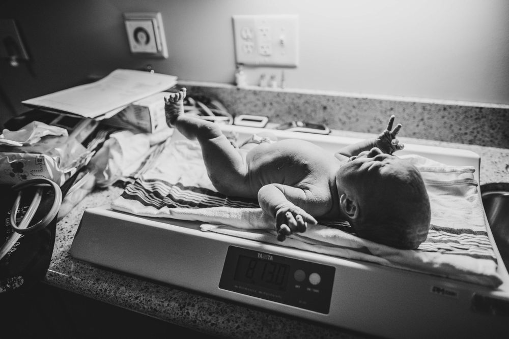 Black and white image of newborn sleeping on medical scale.