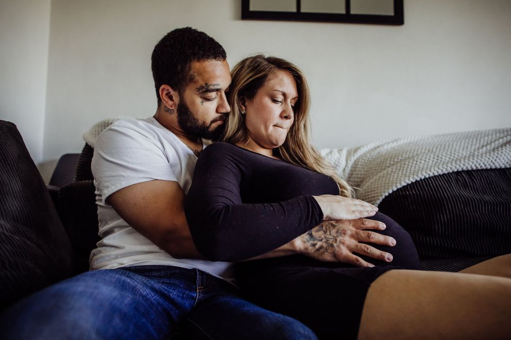 Couple relaxing on couch during intimate maternity photography session.