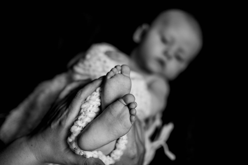 Close up black and white image of tiny baby feet wrapped in soft fabric.