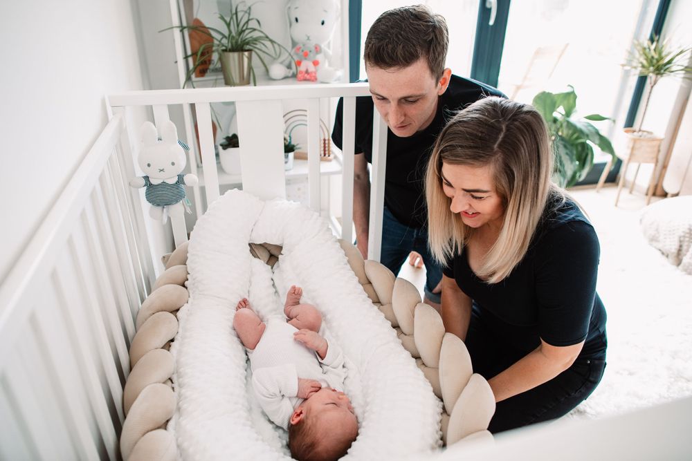 Couple in black outfits smiling while looking down at their baby in a white crib.