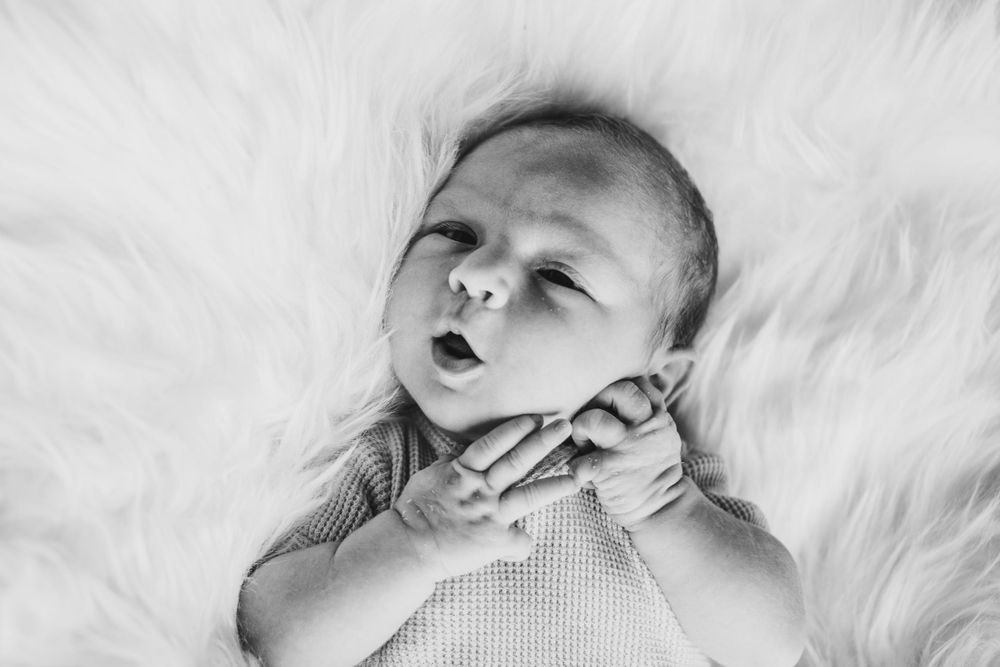 Close-up black and white photo of a baby lying on fluffy white textured surface.