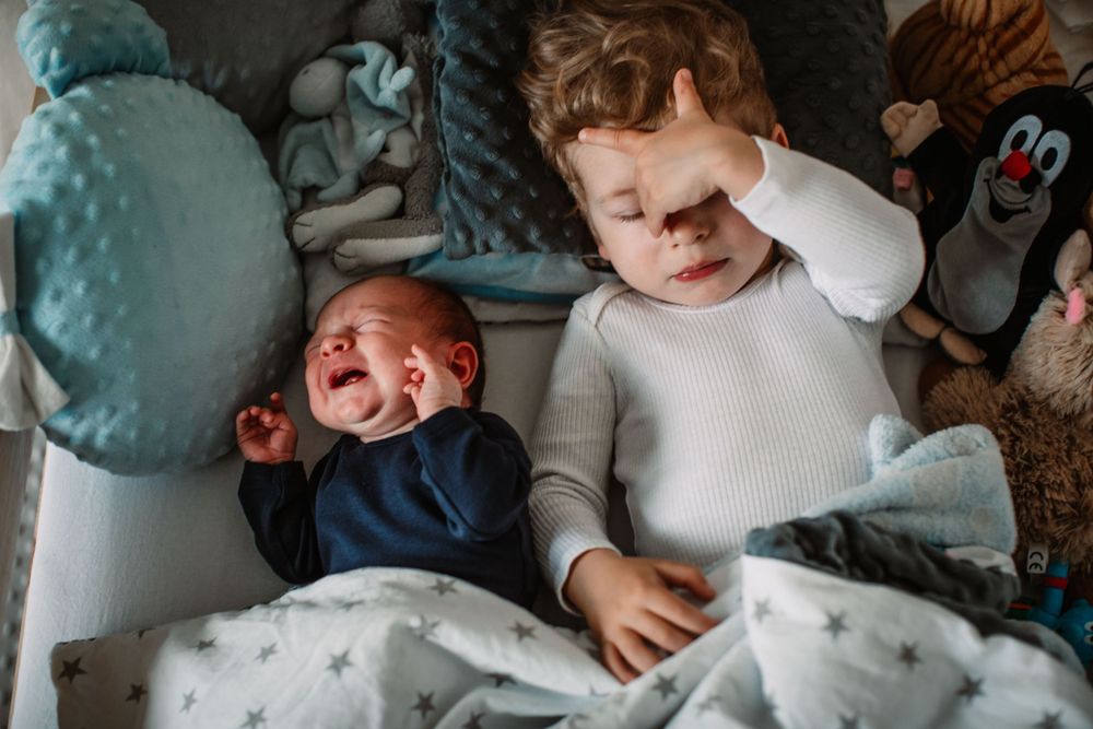 Two children on bed with stuffed toys, one crying while other covers face.