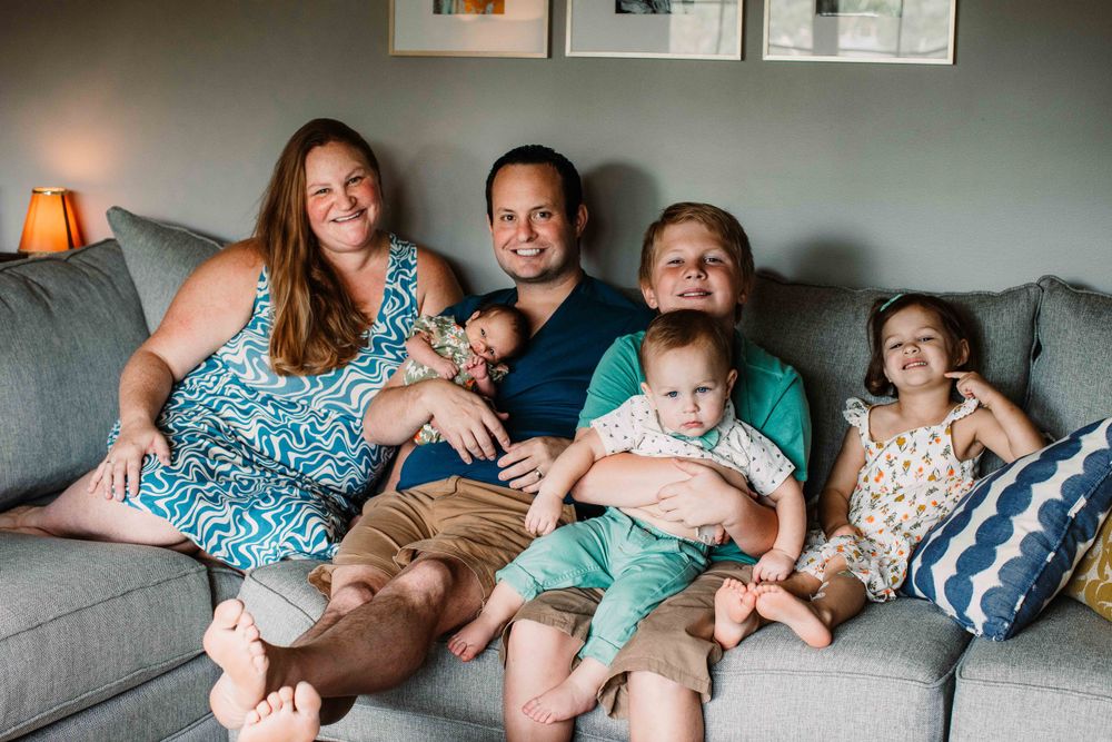 A family relaxes together on a grey couch in their living room.