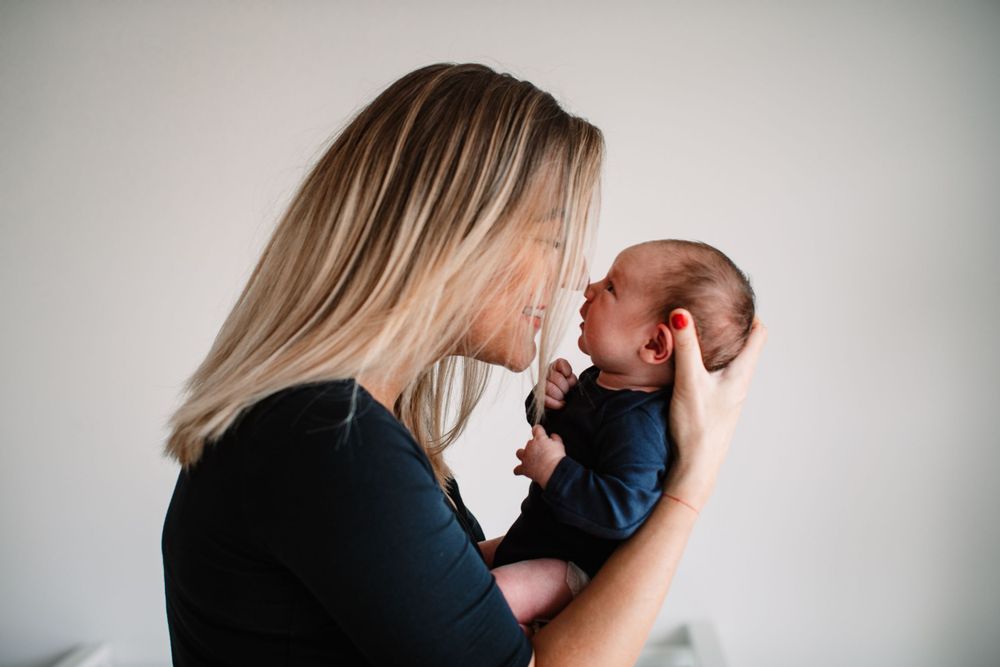 Intimate moment between parent and newborn against neutral backdrop.