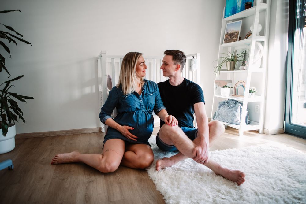 Couple sitting on white plush rug in nursery with modern decor and plants.