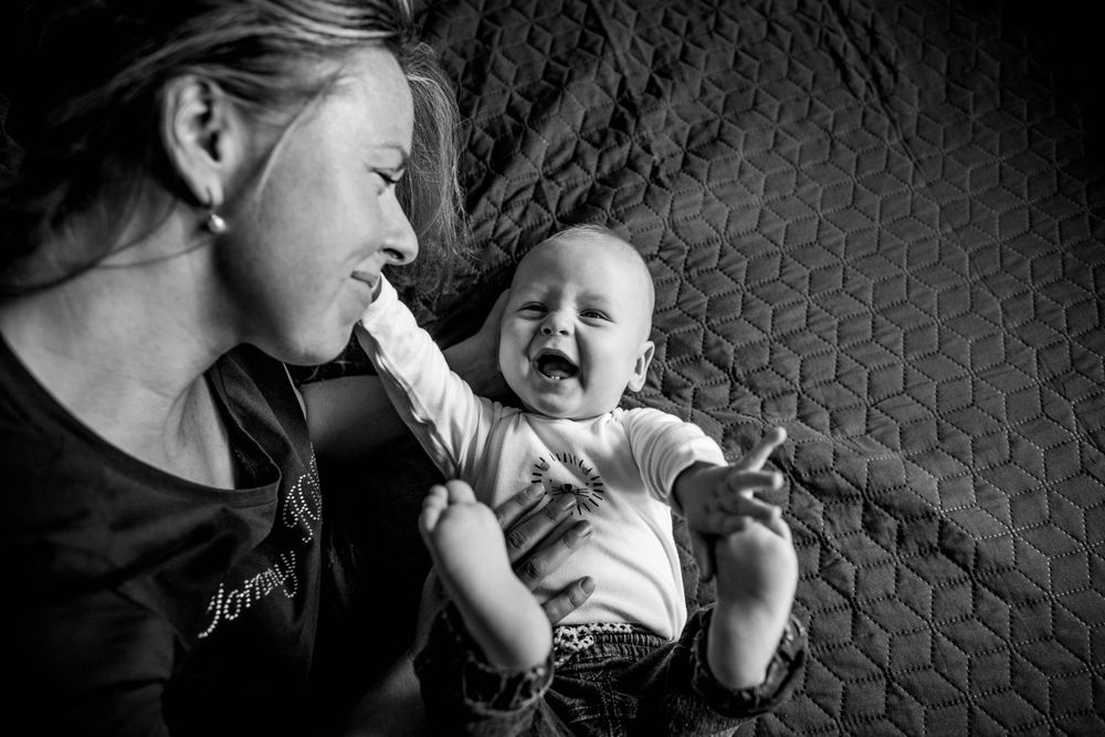 Black and white portrait of joyful baby interacting with caregiver against patterned background.