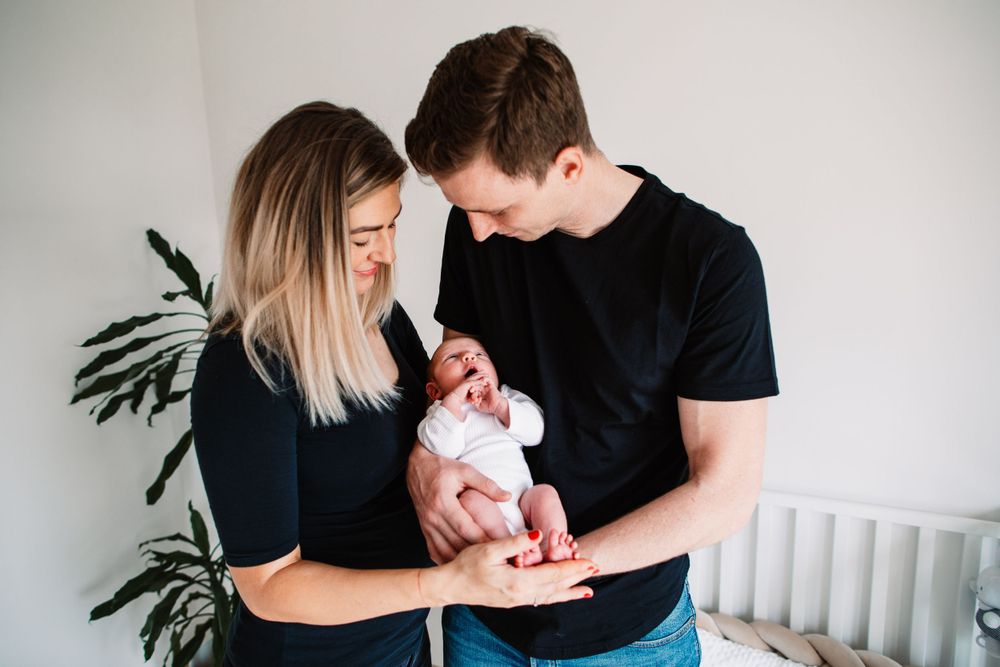 New parents sharing a tender moment with their newborn baby while standing near a houseplant.