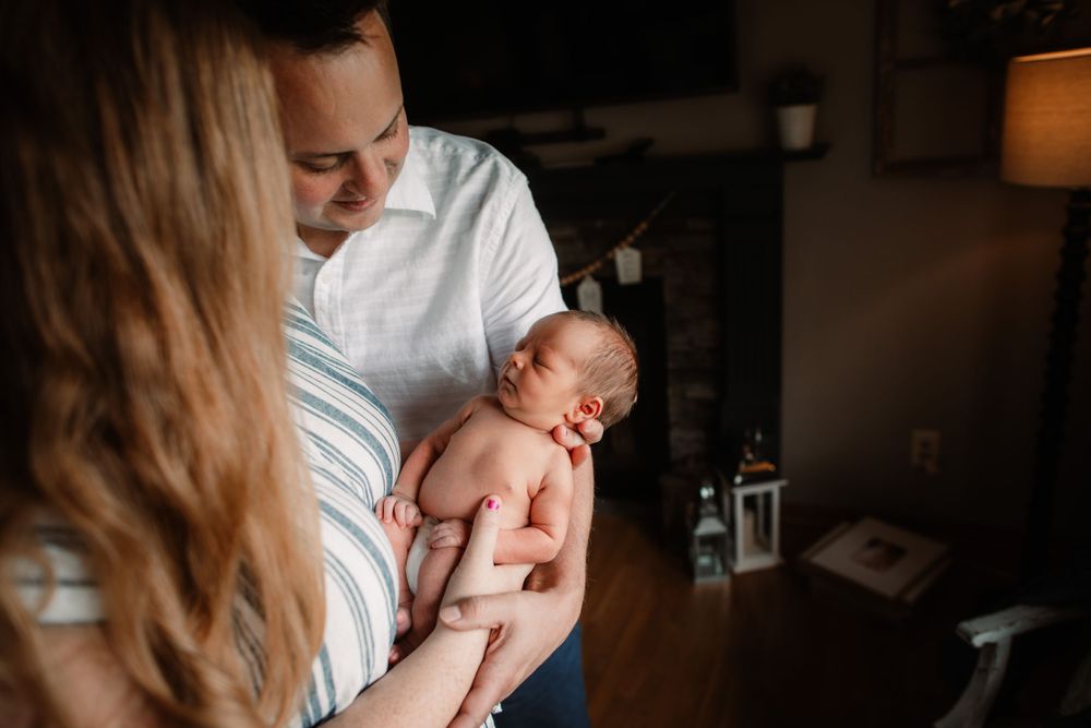Tender moment between parents holding newborn baby in dimly lit room with warm ambient lighting.