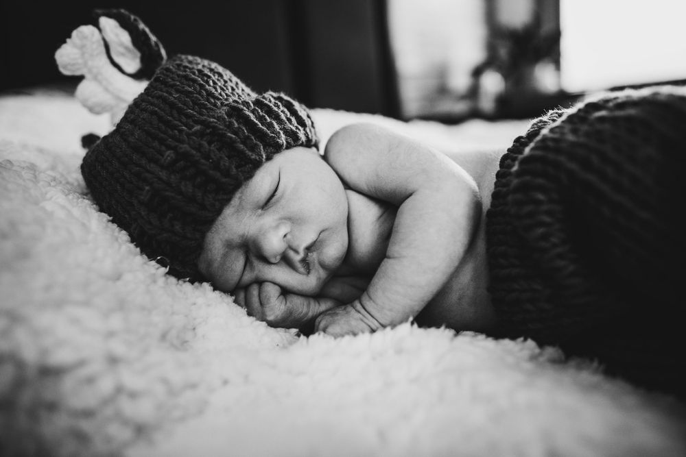 Black and white portrait of peaceful sleeping baby wearing knit hat on soft blanket.