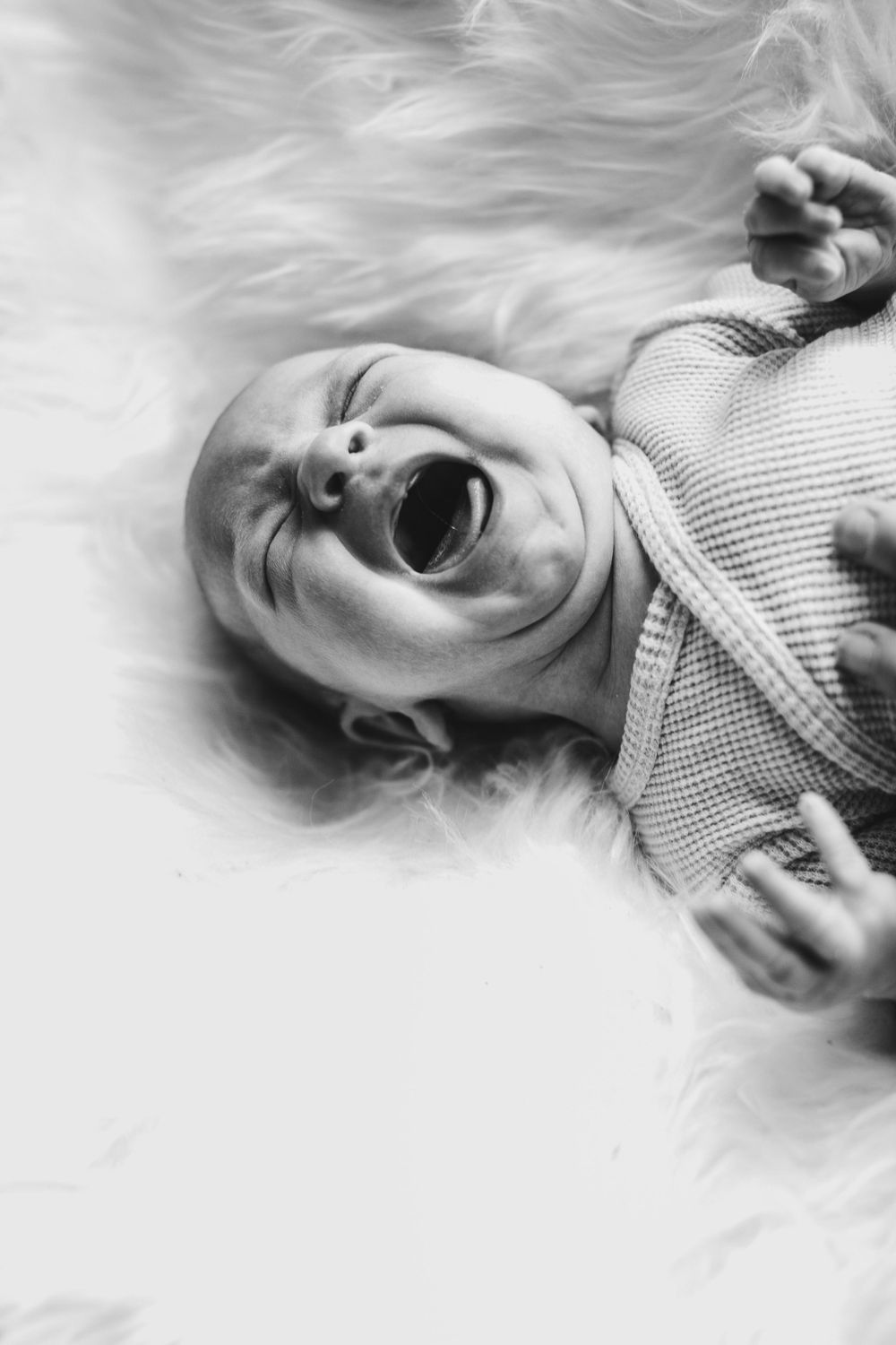 Black and white portrait of a crying baby lying on soft white fur.