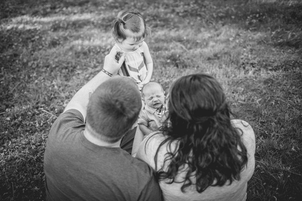 Family sitting together on grass viewing their newborn baby from above.