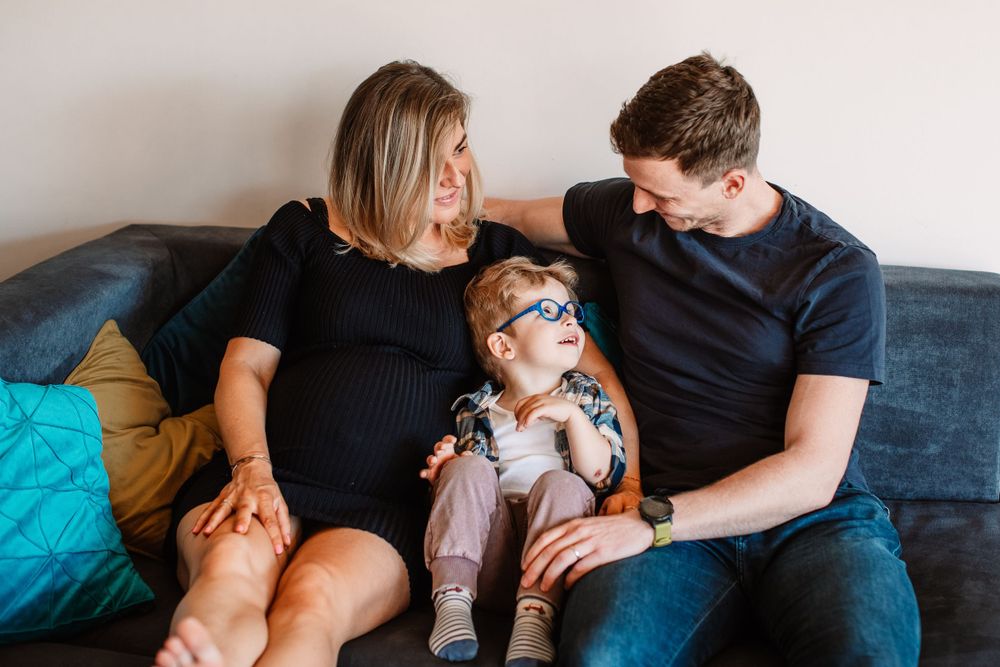 Family lounging on navy couch with toddler wearing sunglasses.
