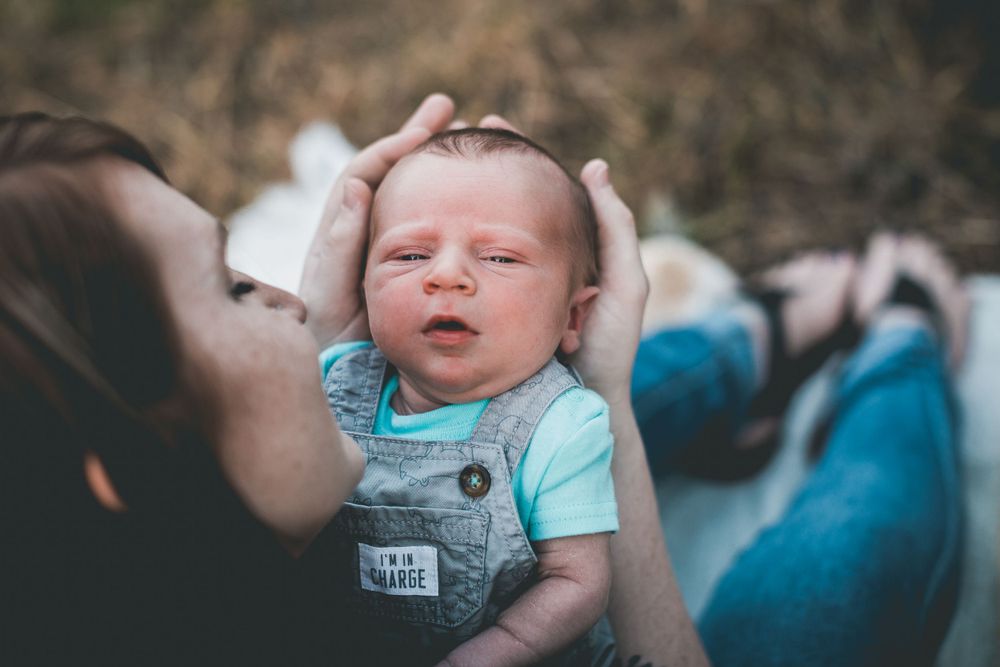 Baby in light blue onesie held up against sunny outdoor background.