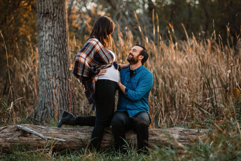 Couple sharing intimate moment during maternity photoshoot in outdoor fall setting.