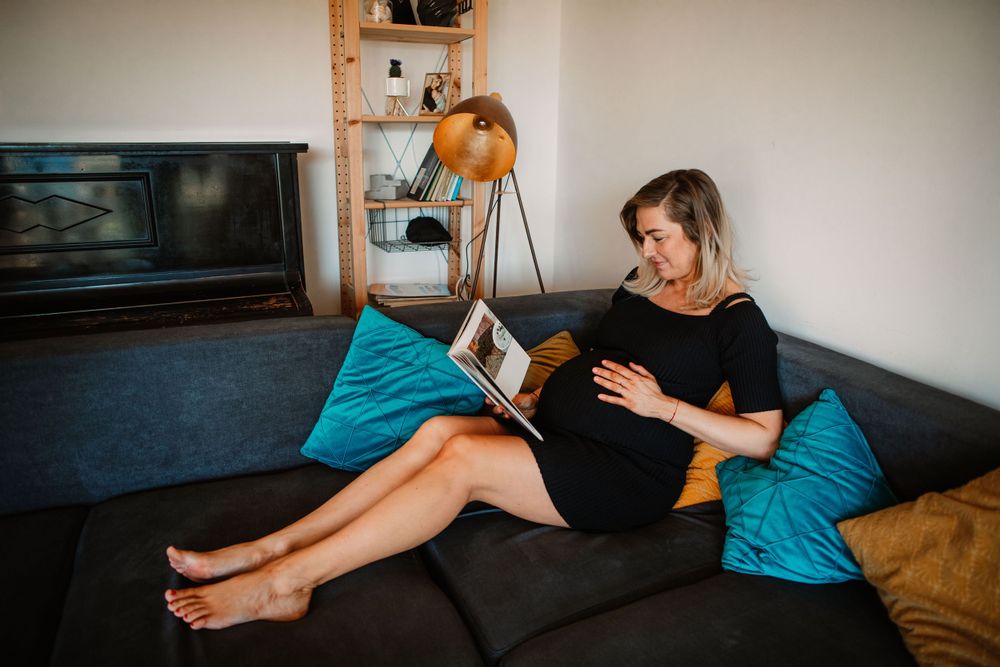 Pregnant woman relaxing on blue couch while reading book.