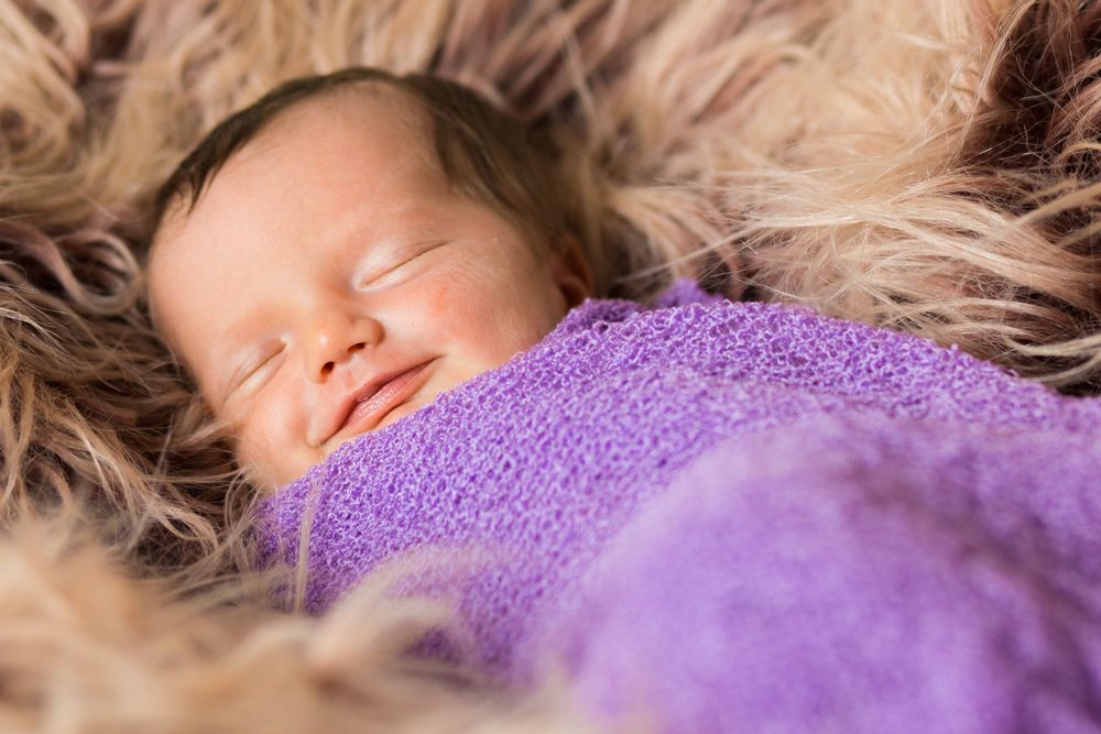 Sleeping baby wrapped in purple blanket on furry background.