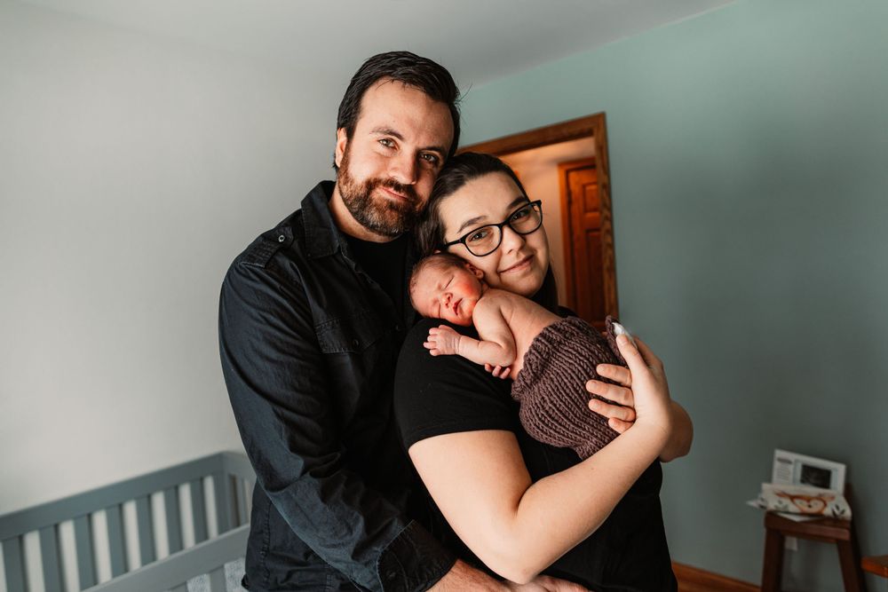Intimate family portrait in nursery with baby wrapped in brown knit blanket.