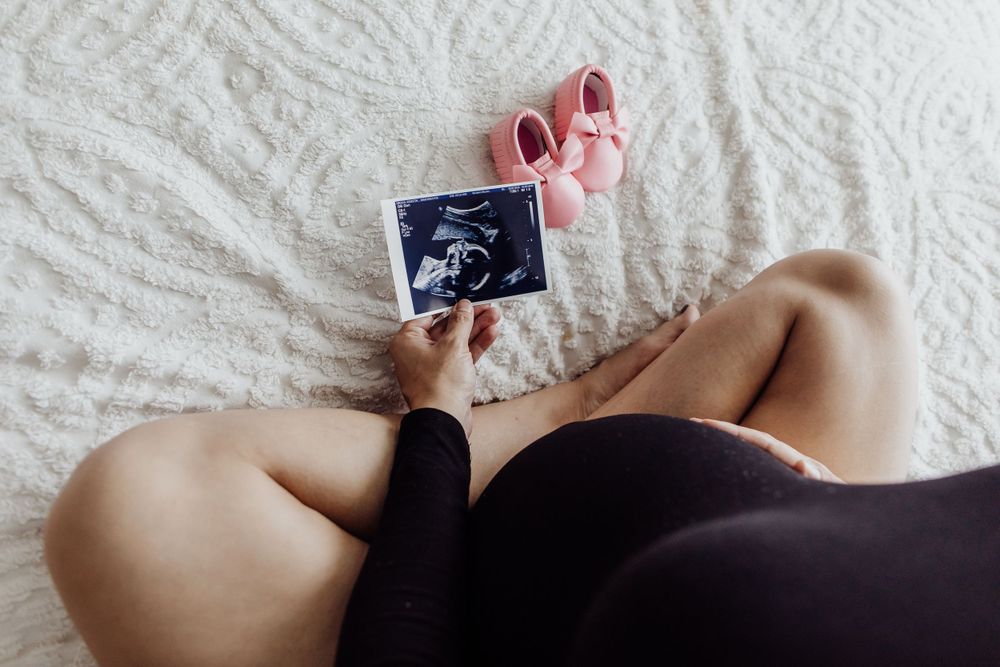 Person holding ultrasound photo against white bedding with soft pink accents.