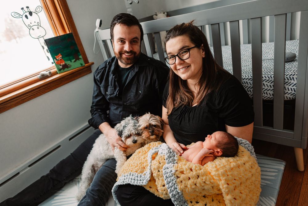 New parents with infant and dog sitting together in cozy nursery setting.