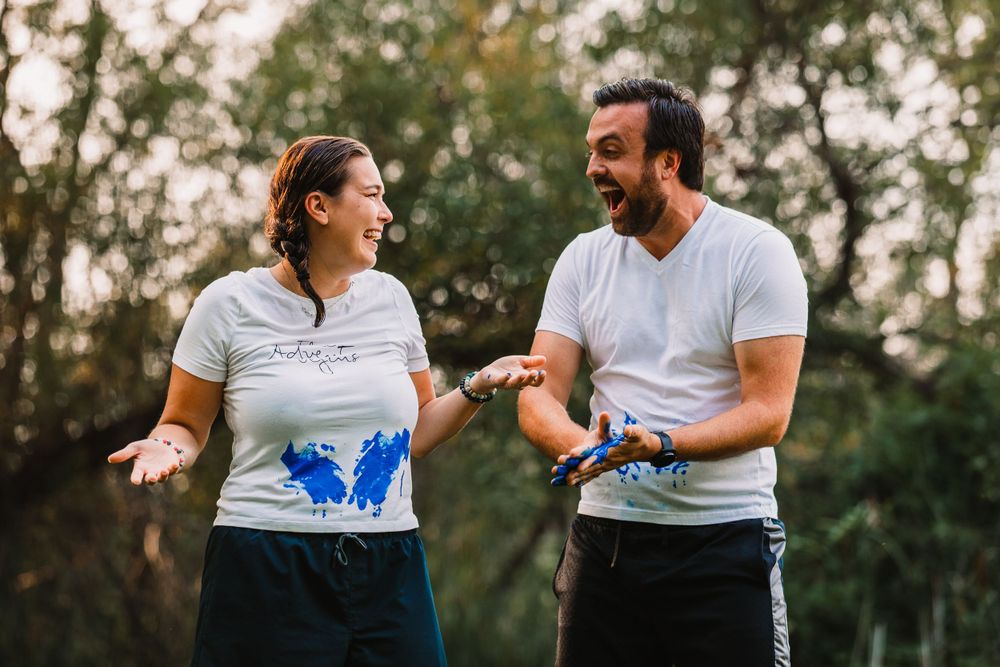 Couple in white shirts showing messy blue paint on their hands during a gender reveal photoshoot.