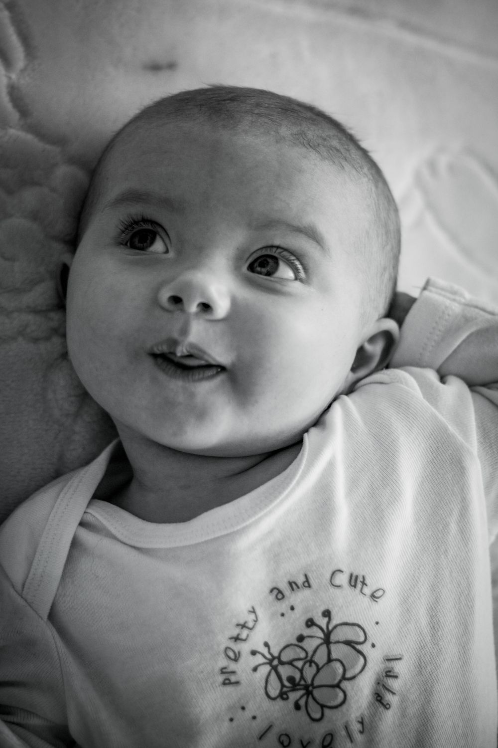 A black and white portrait of an infant wearing a white onesie with a cute smile.