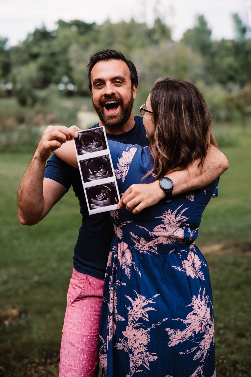 Joyful couple holding ultrasound photos in an outdoor setting.