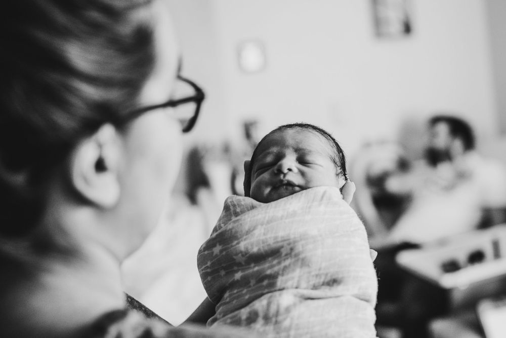 Black and white image of a swaddled crying newborn baby being held.