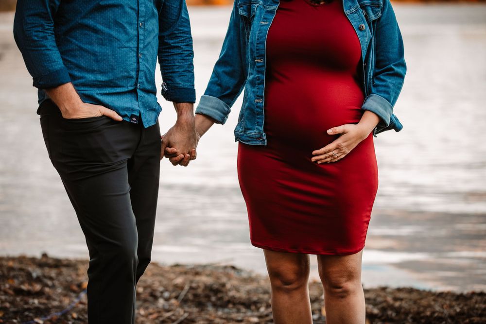 Couple holding hands with focus on pregnant belly in red dress and denim jacket.