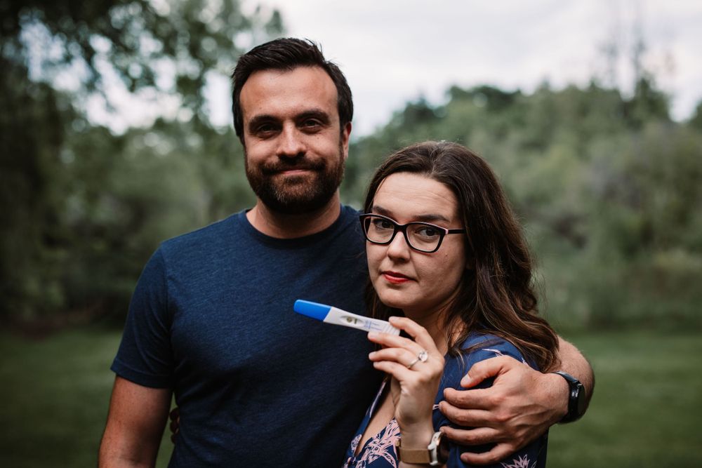 Couple in casual attire celebrating with a positive pregnancy test result in an outdoor garden setting.