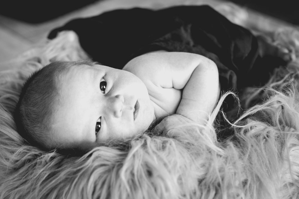 Black and white image of baby lying on furry blanket with alert expression.