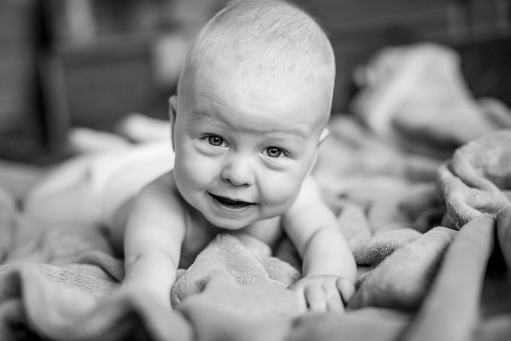 Baby lying on blankets smiles at camera in black and white portrait.