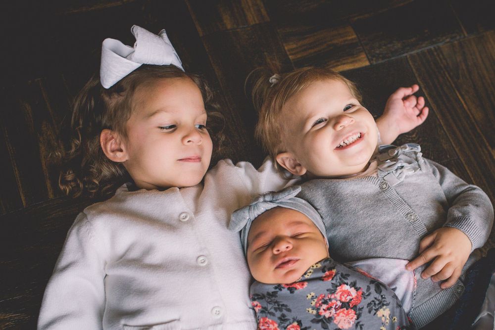 Three siblings pose together with newborn baby in the middle.