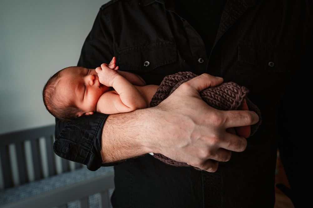 A sleeping newborn nestled securely in caring arms wearing a knit outfit.