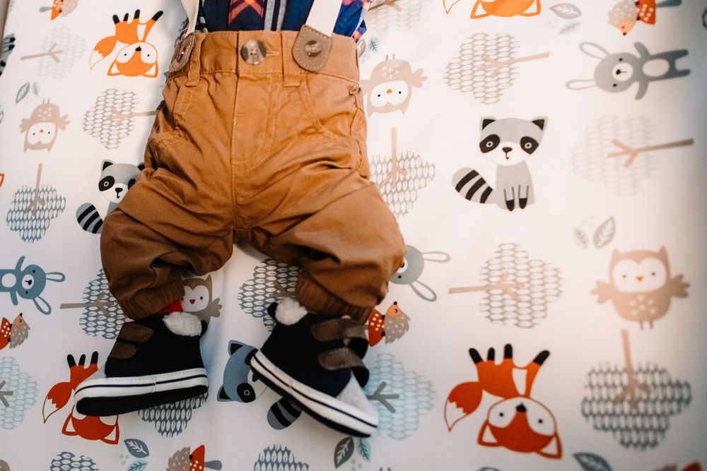 Close-up of brown baby pants and shoes on whimsical animal print crib sheets.
