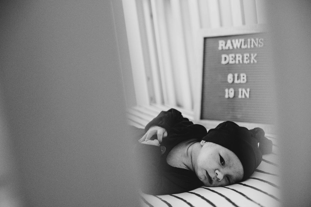Black and white photo of person resting in crib with measurement board visible.