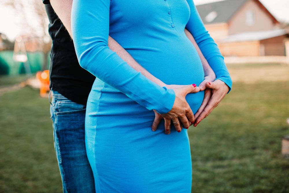 Pregnancy photo showing embrace with hands forming heart shape on bright blue maternity dress.