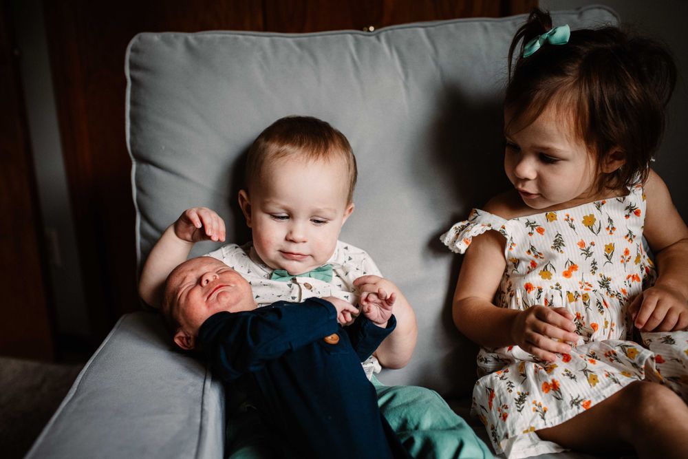 Two young children sitting together on gray couch cushion.