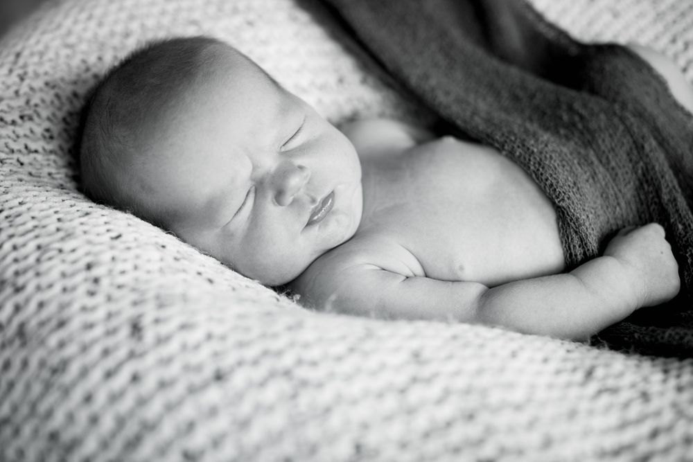 Peaceful black and white portrait of sleeping newborn on textured blanket.
