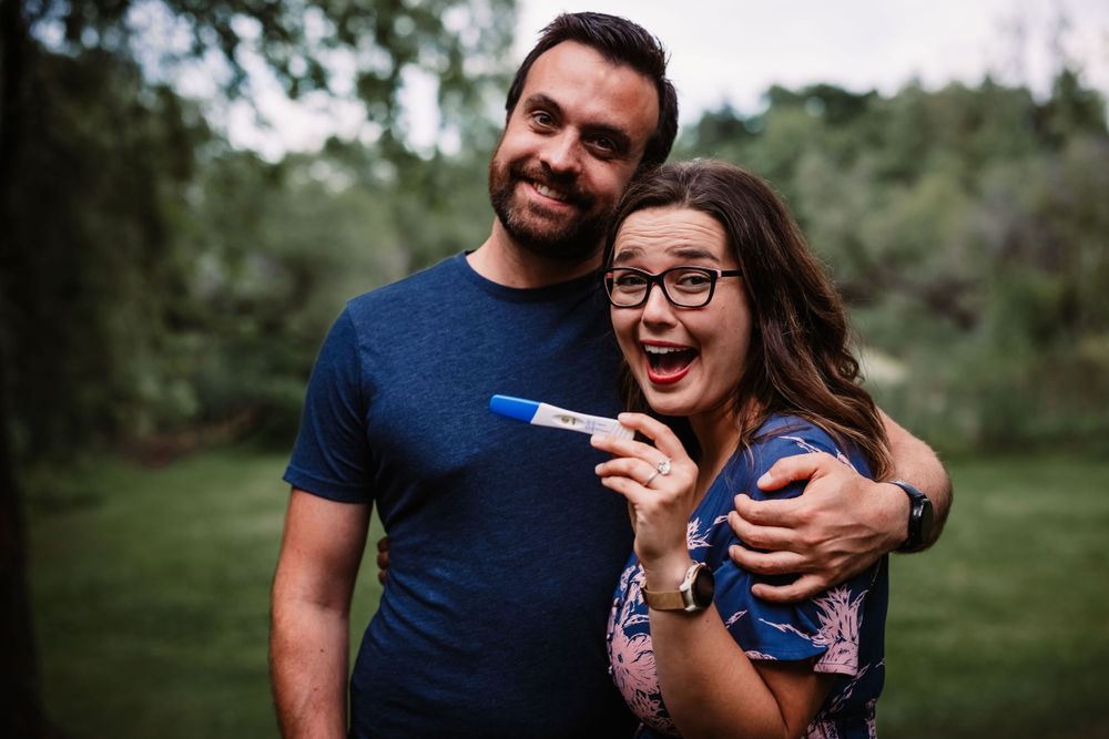 Excited couple embracing while holding a positive pregnancy test in a natural outdoor setting.