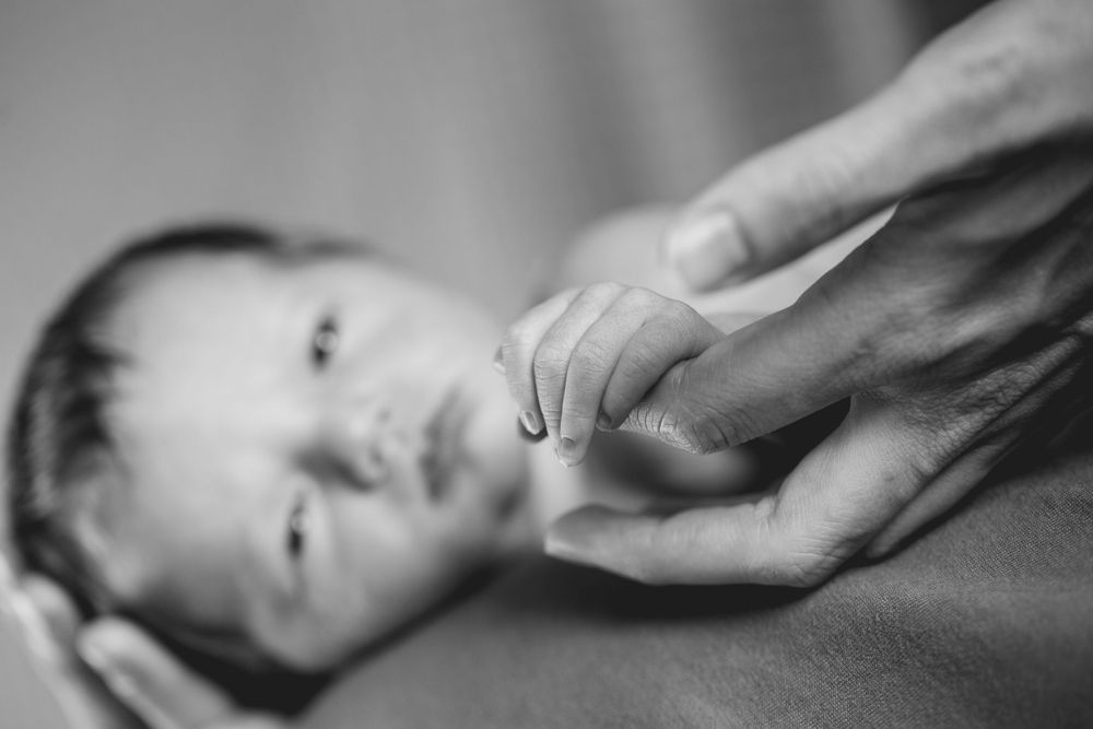 Black and white close-up of small hand grasping adult finger.