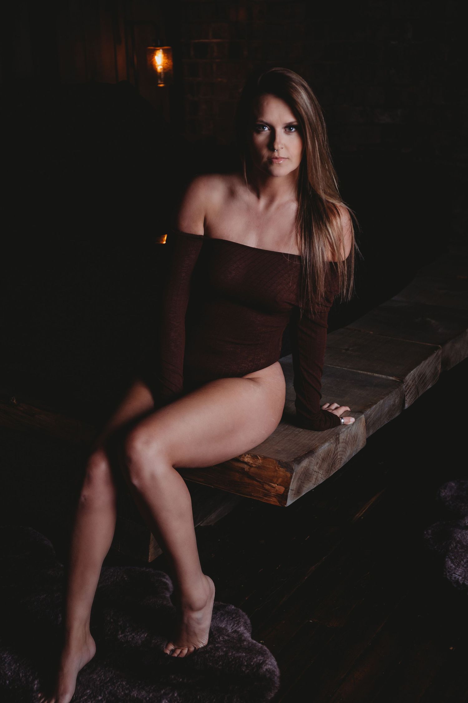 Dark moody boudoir photoshoot on wooden bench with candlelight.