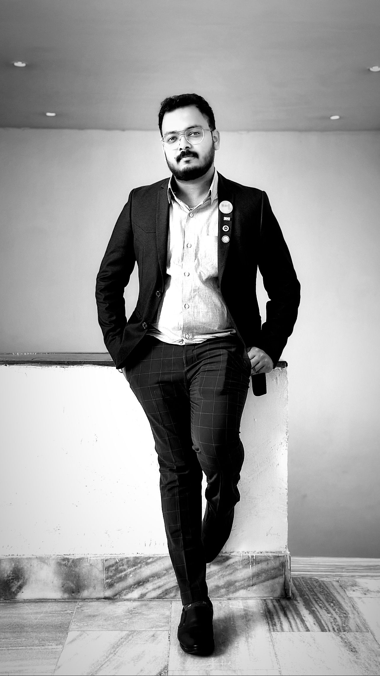 Professional portrait of a person in a dark suit and white shirt posing against a light wall.