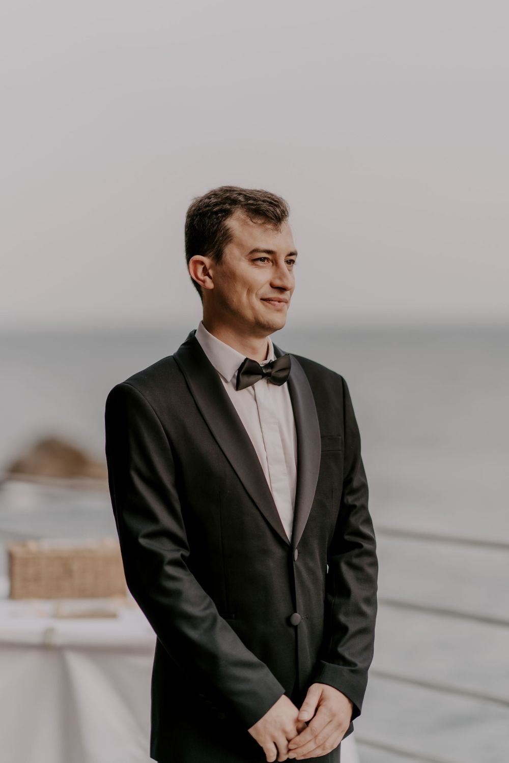 Man in formal black tuxedo at seaside wedding venue.