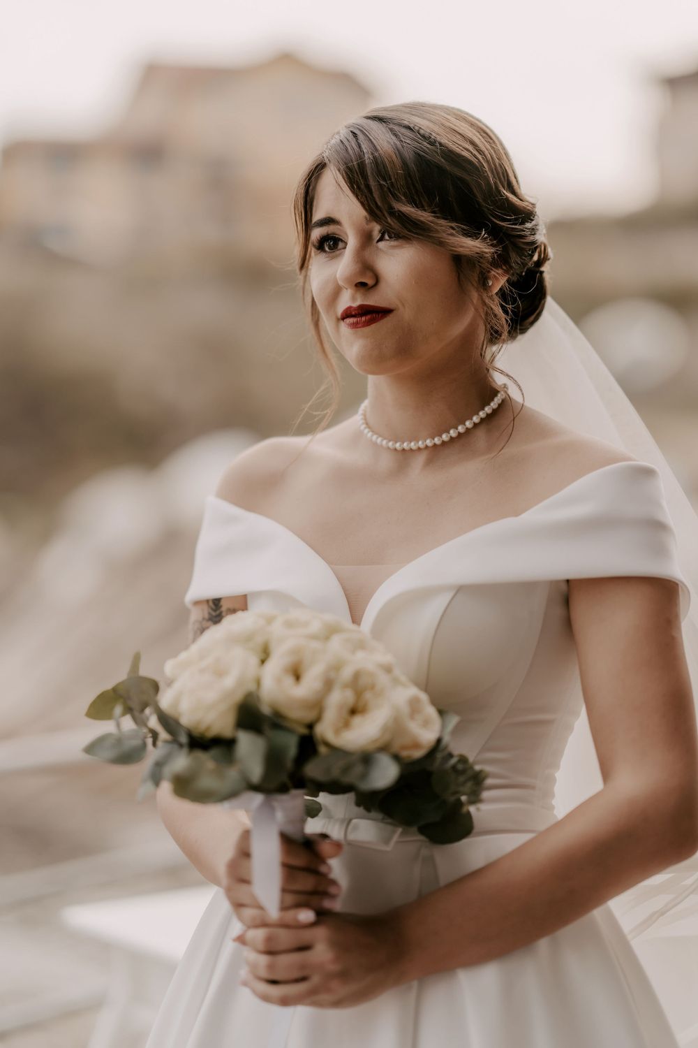 Close-up details of bride holding classic white rose bouquet in elegant off-shoulder wedding dress.