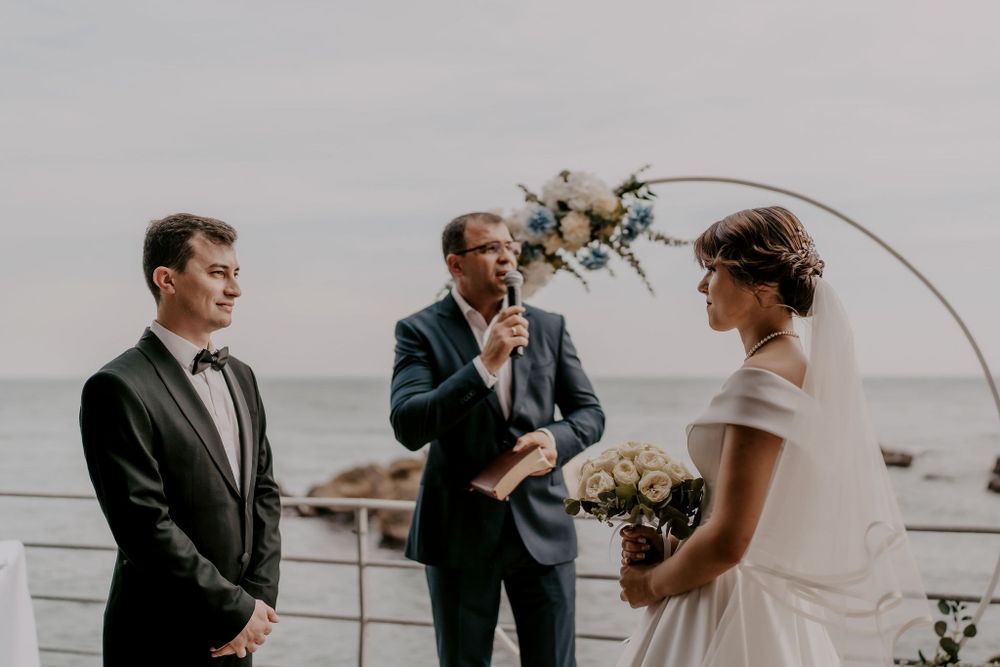 Waterfront wedding ceremony with decorative arch and natural coastal backdrop.