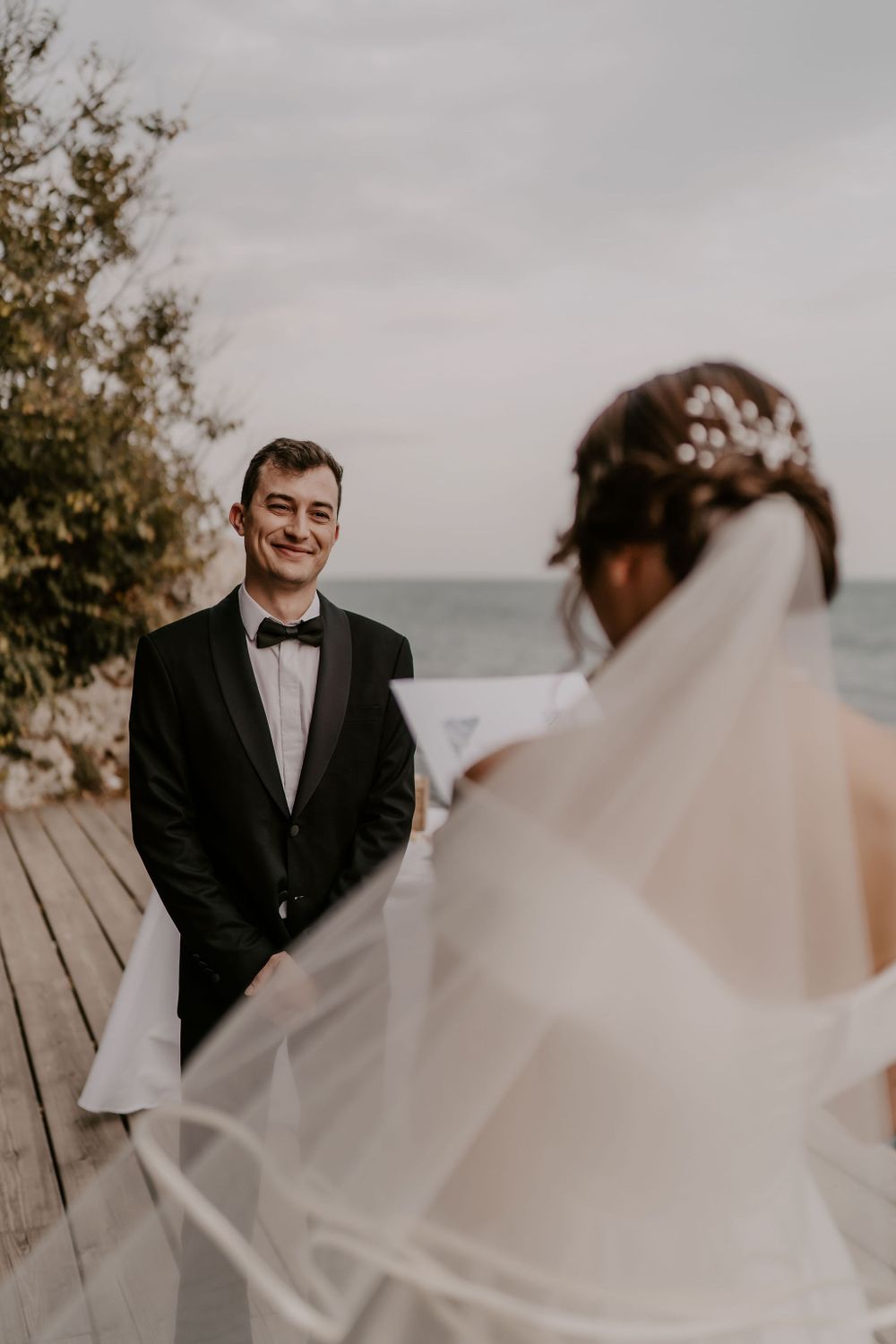 A couple shares a first look moment on a wooden deck overlooking the ocean during their wedding ceremony.