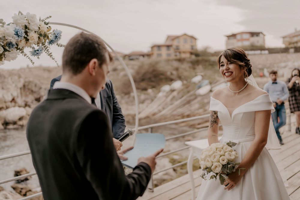 A couple exchanges vows during their waterfront wedding ceremony on a wooden boardwalk.